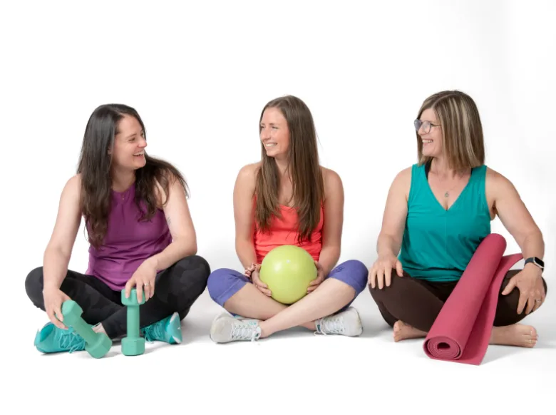 Three Studio IPF members sitting together with weights, a ball, and a yoga mat